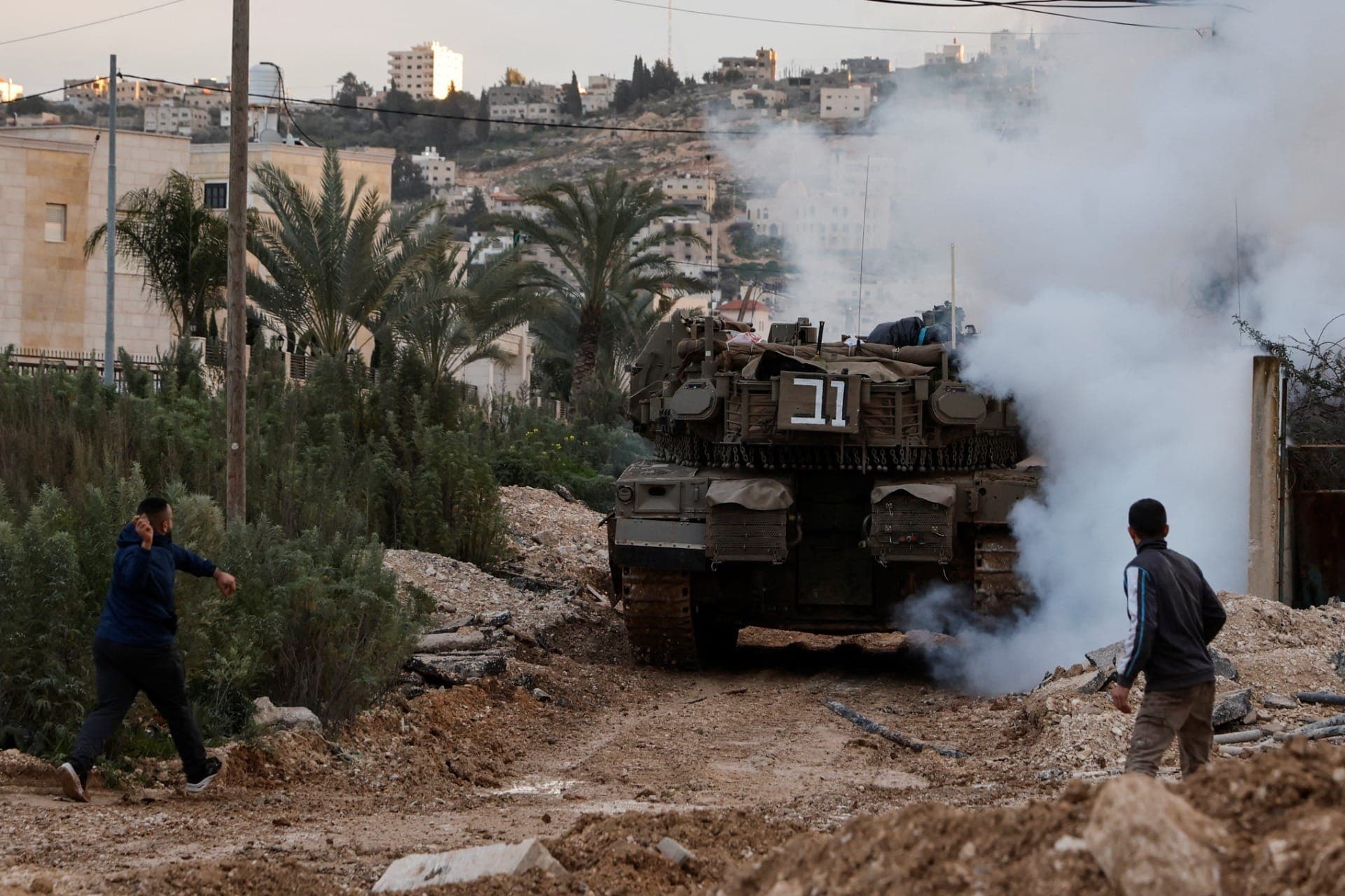 Homem se prepara para atirar um objeto enquanto um tanque israelense na Cisjordânia