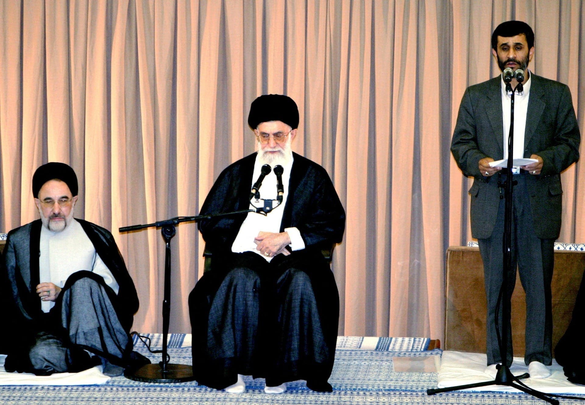 Mahmoud Ahmadinejad em pé. Ao centro, o então aiatolá Ali Khamenei