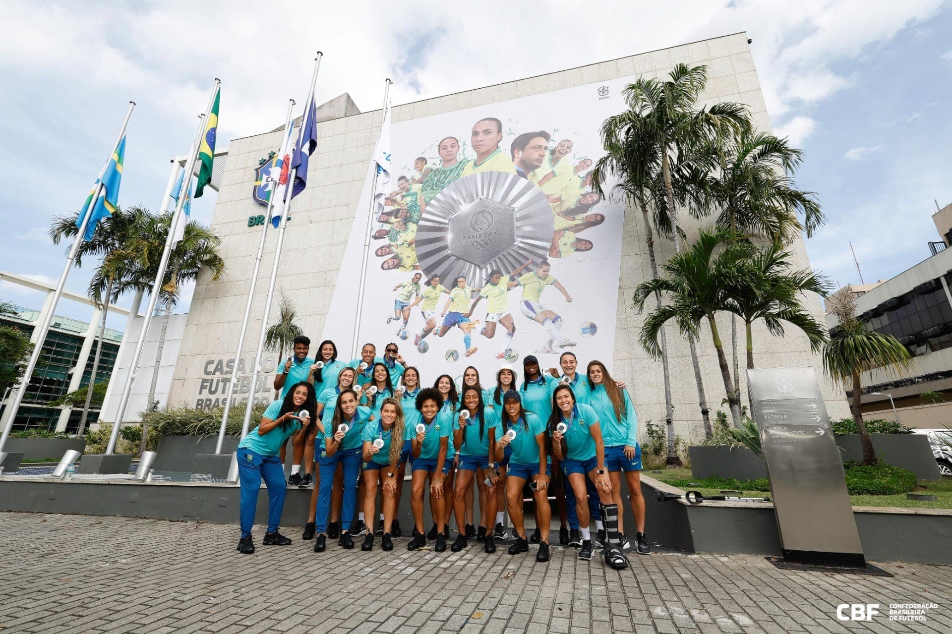 Seleção feminina posa com a medalha de prata em frente ao painel na CBF